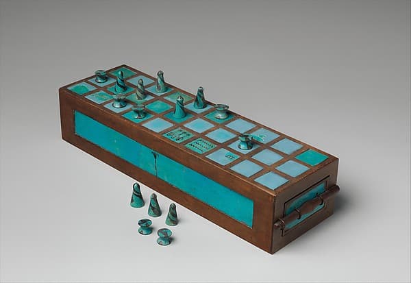 A blue-green faience game board with its set of gaming pieces, some standing on the ruled squares and others beside the board